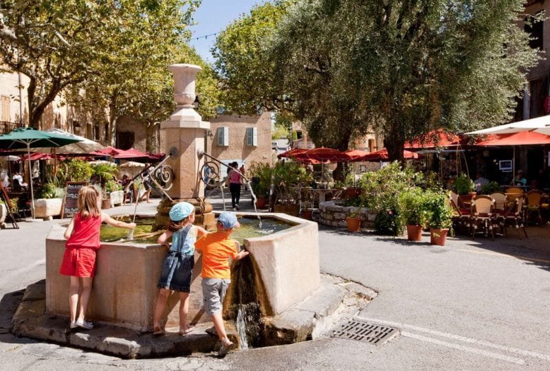 Children playing with water from the fountain in the centre of a small Provencal village